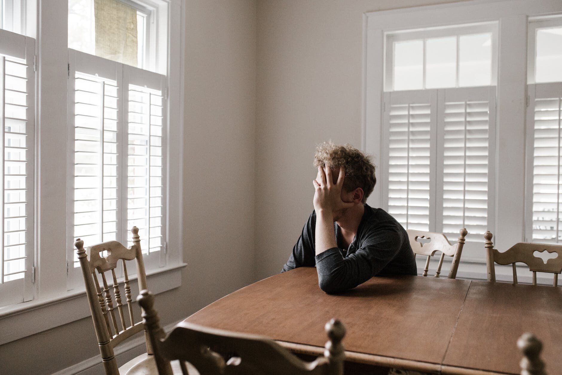 Imagen de un hombre sentado en el comedor de su casa, recargado en la mesa, sujetando su rostro, preocupado por garantizar el futuro de su familia, en la sección de Seguros de Vida del Sitio Web de Gilberto Fahara Consultores en Seguros..